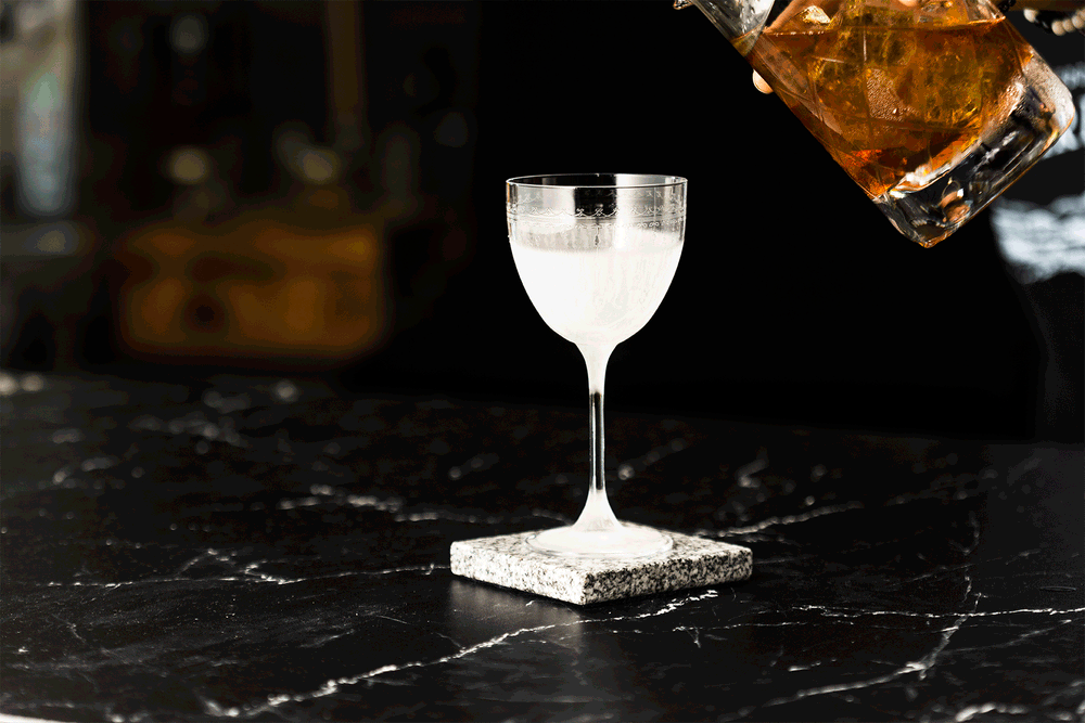 Negroni cocktail being poured in a glass and garnished with a lemon