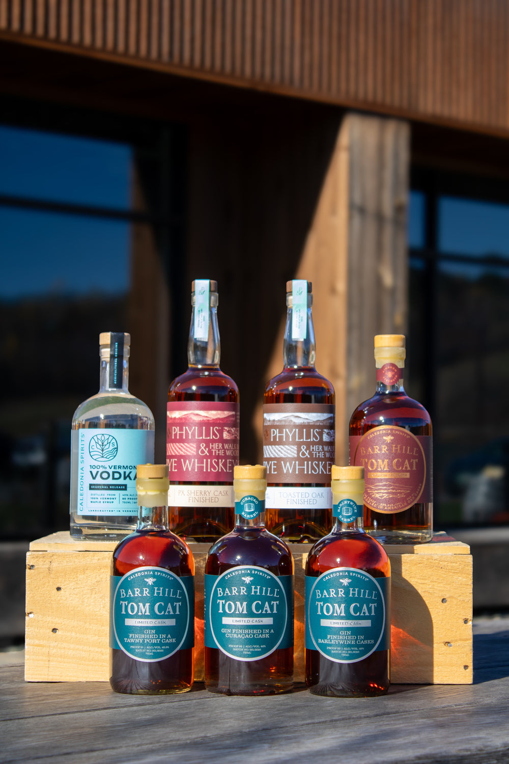 Collection of liquor bottles on a wooden crate with a blurred outdoor background