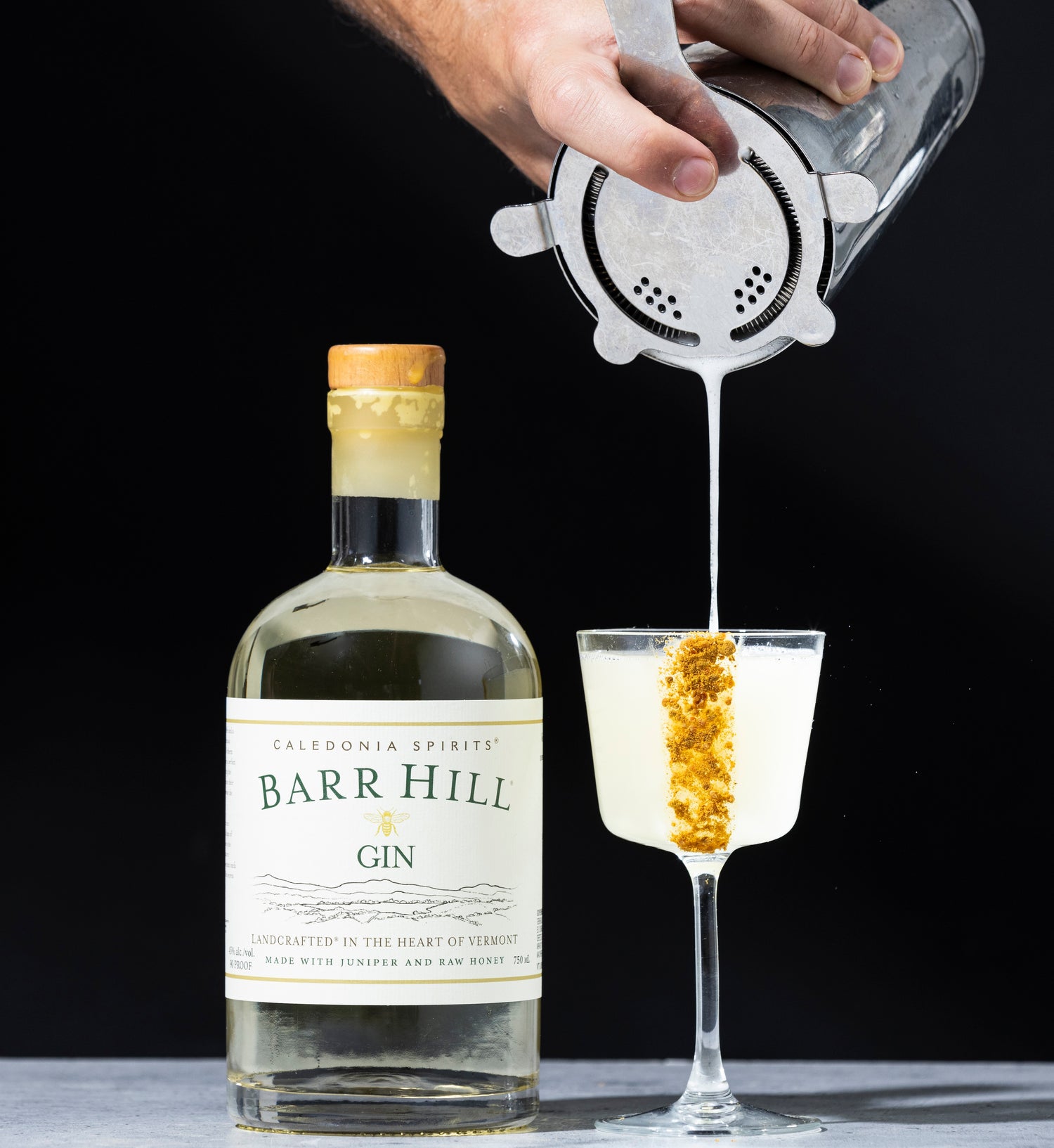 Bottle of Barr Hill Gin with a cocktail being poured into a glass.