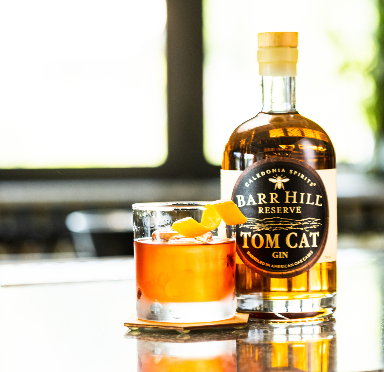 Bottle of Barr Hill Reserve Tom Cat Gin with a negroni cocktail on a table.