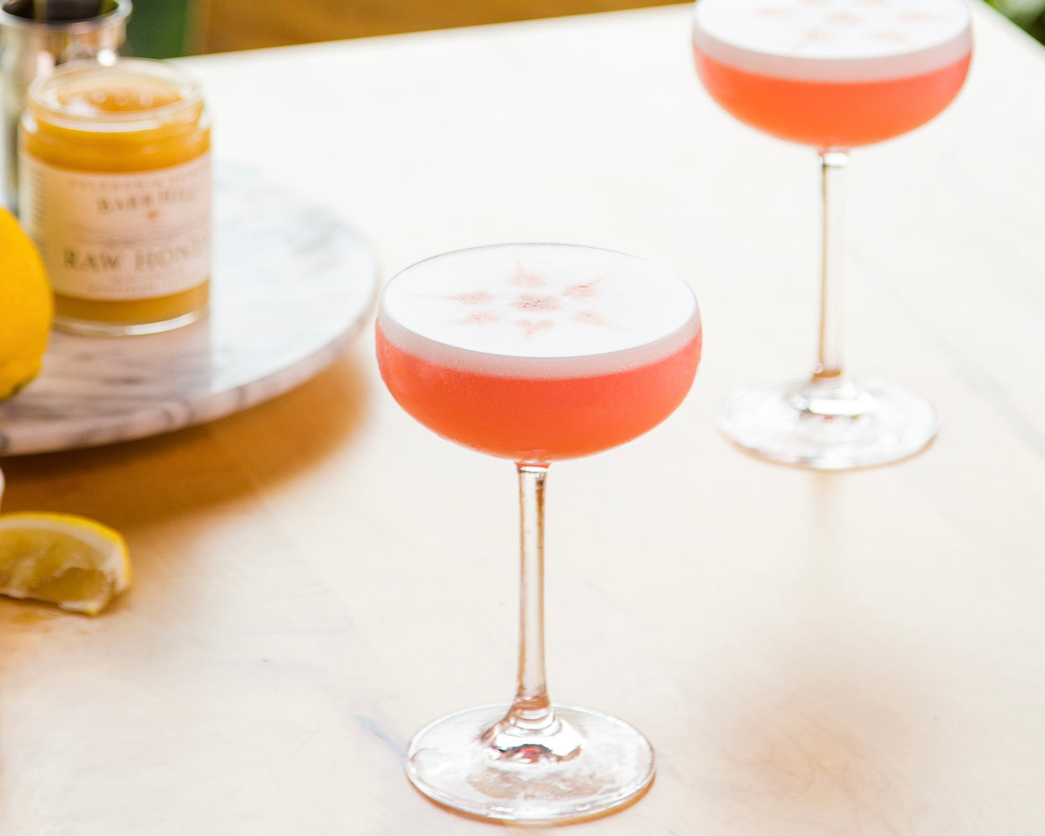 Two pink negroni cocktails in highball glasses on a white surface with a lemon wedge.